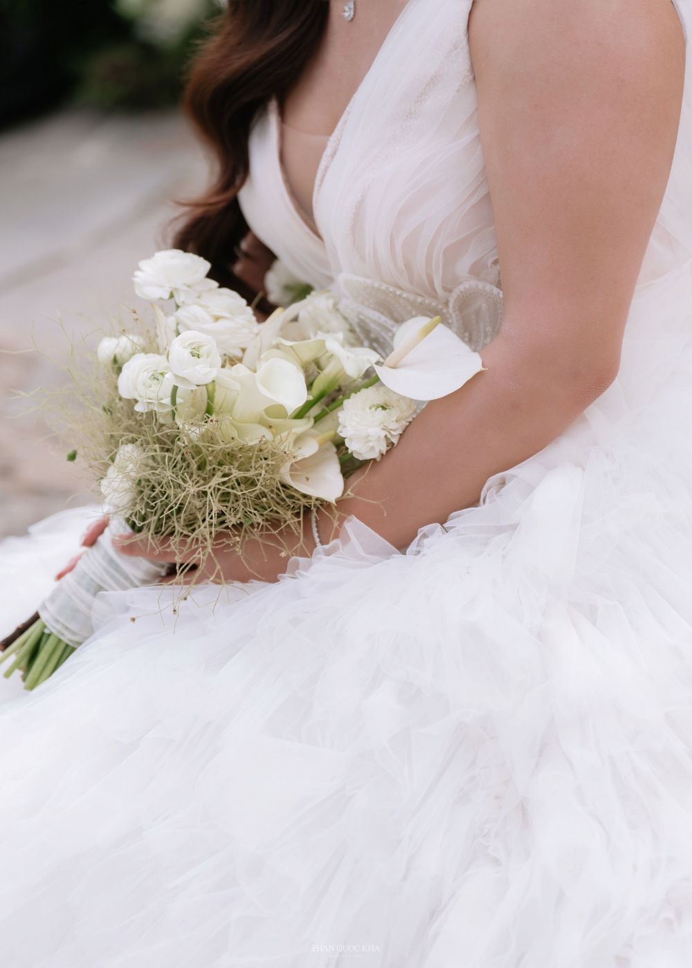 Close-up of a bride in a white ruffled gown holding an elegant bouquet of white calla lilies.