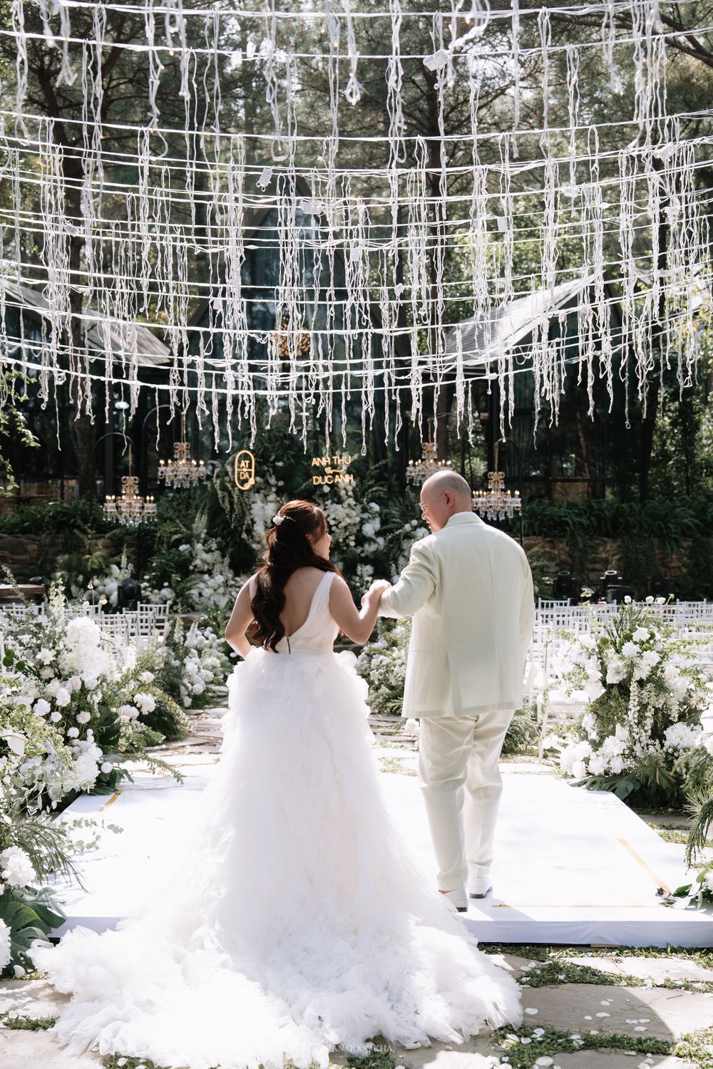 Bride and groom standing at altar beneath stunning hanging crystal decorations in forest ceremony.