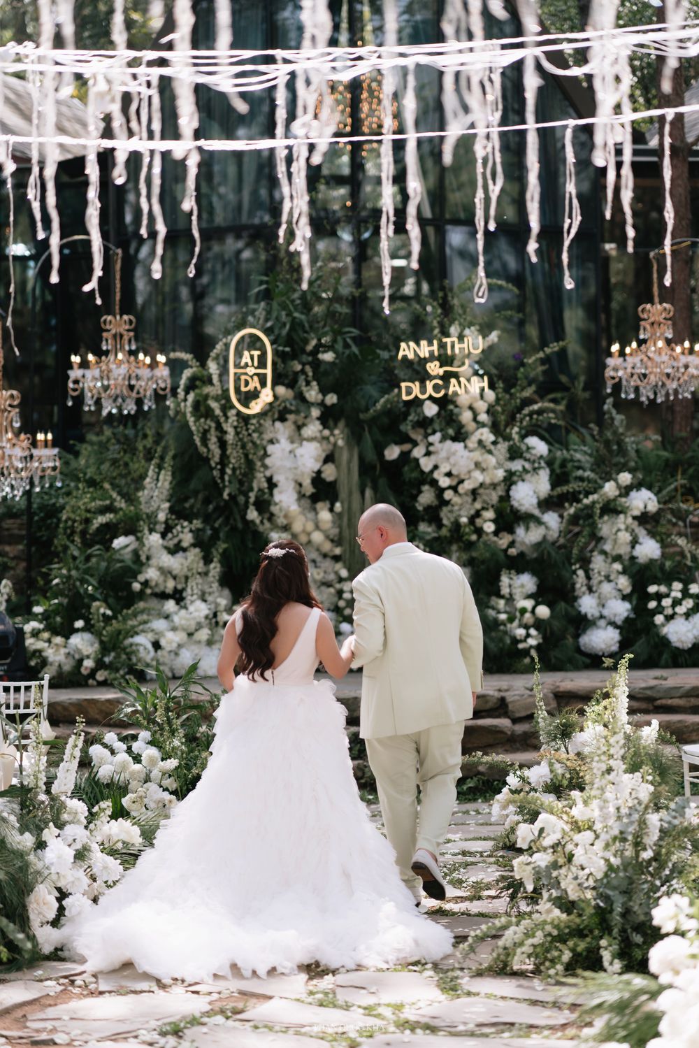Bride and groom walking toward floral altar with glowing neon name sign at forest wedding.