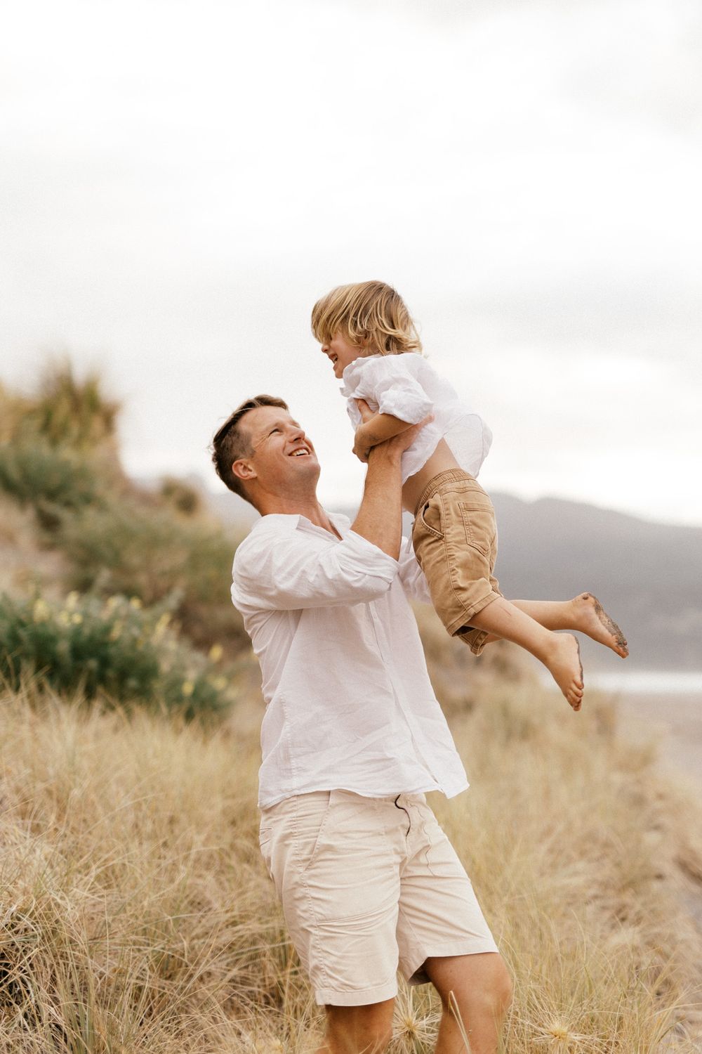 Parent and child share joyful moments together in a golden meadow with mountains in the background.