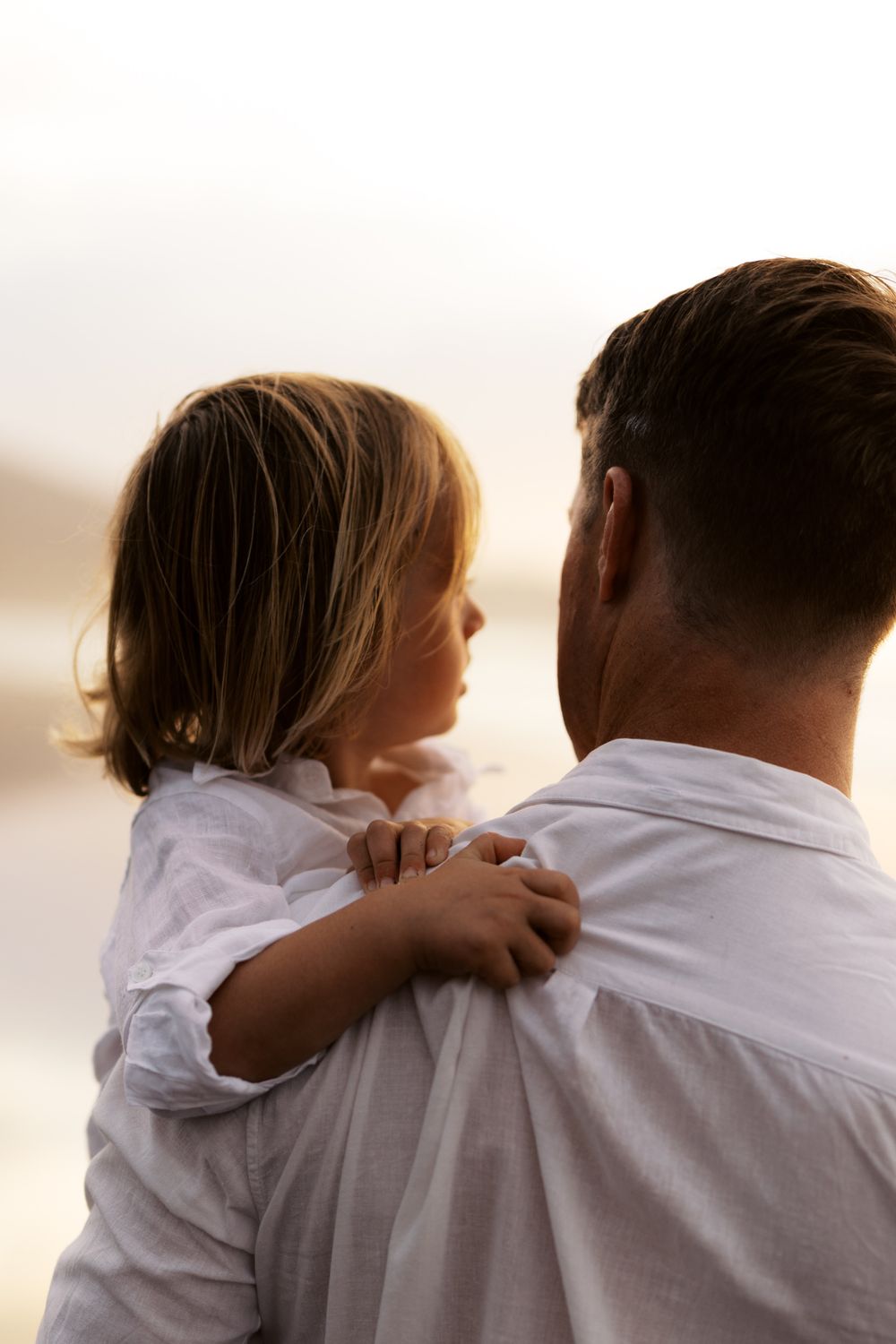 Close-up views of two people wearing white clothing embracing while looking at the ocean.
