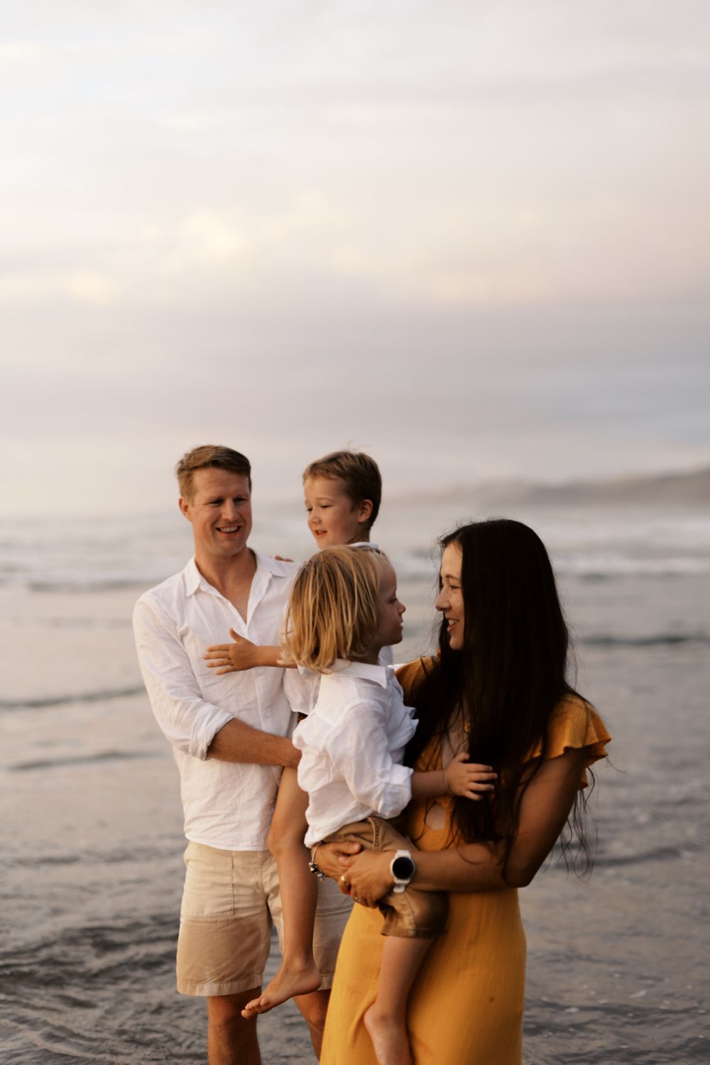 A family wearing white and yellow outfits shares joyful moments together on a cloudy beach.