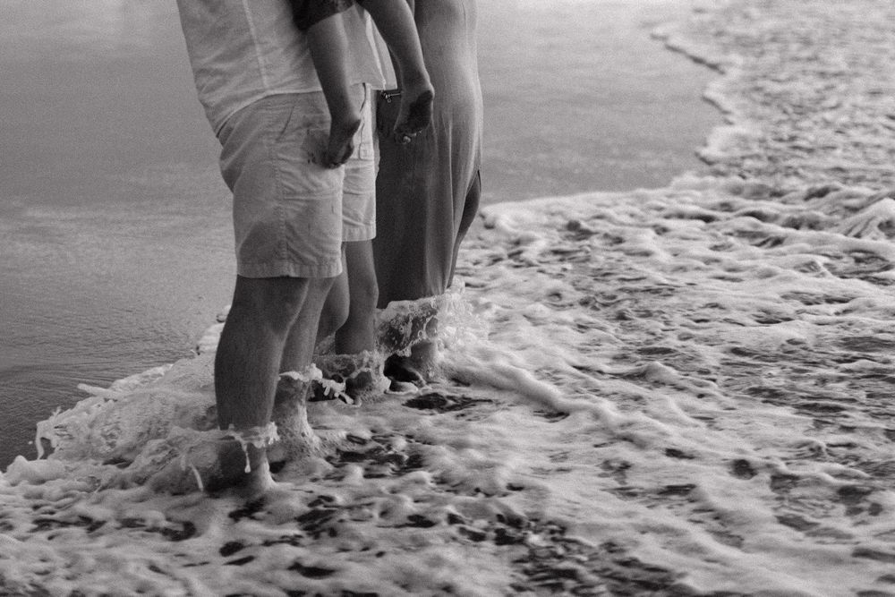 People's feet walking along a sandy beach shore during a leisurely stroll.