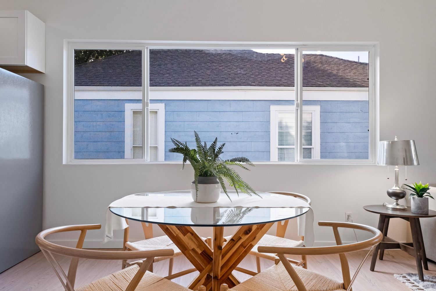 Modern dining room with round glass top table and wooden base near bright windows with ocean view.