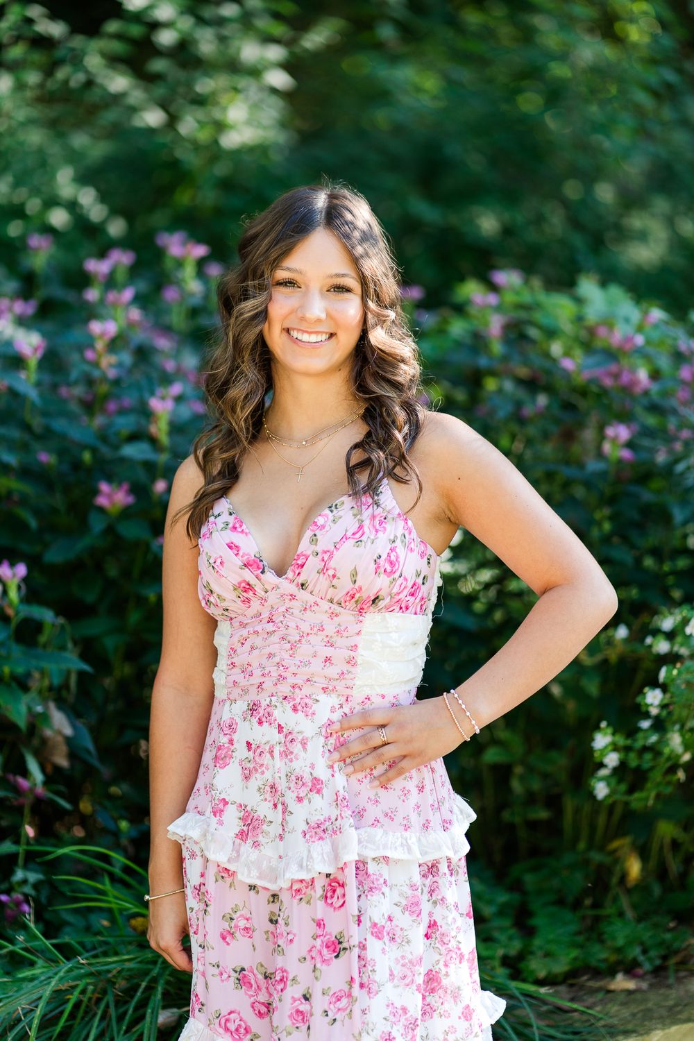A summer portrait in a pink and white floral dress surrounded by garden flowers of a high school senior girl.