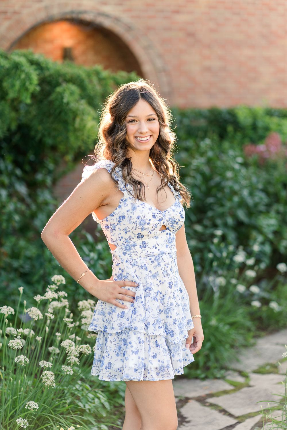 A summer garden photoshoot featuring a blue and white floral top among blooming flowers.