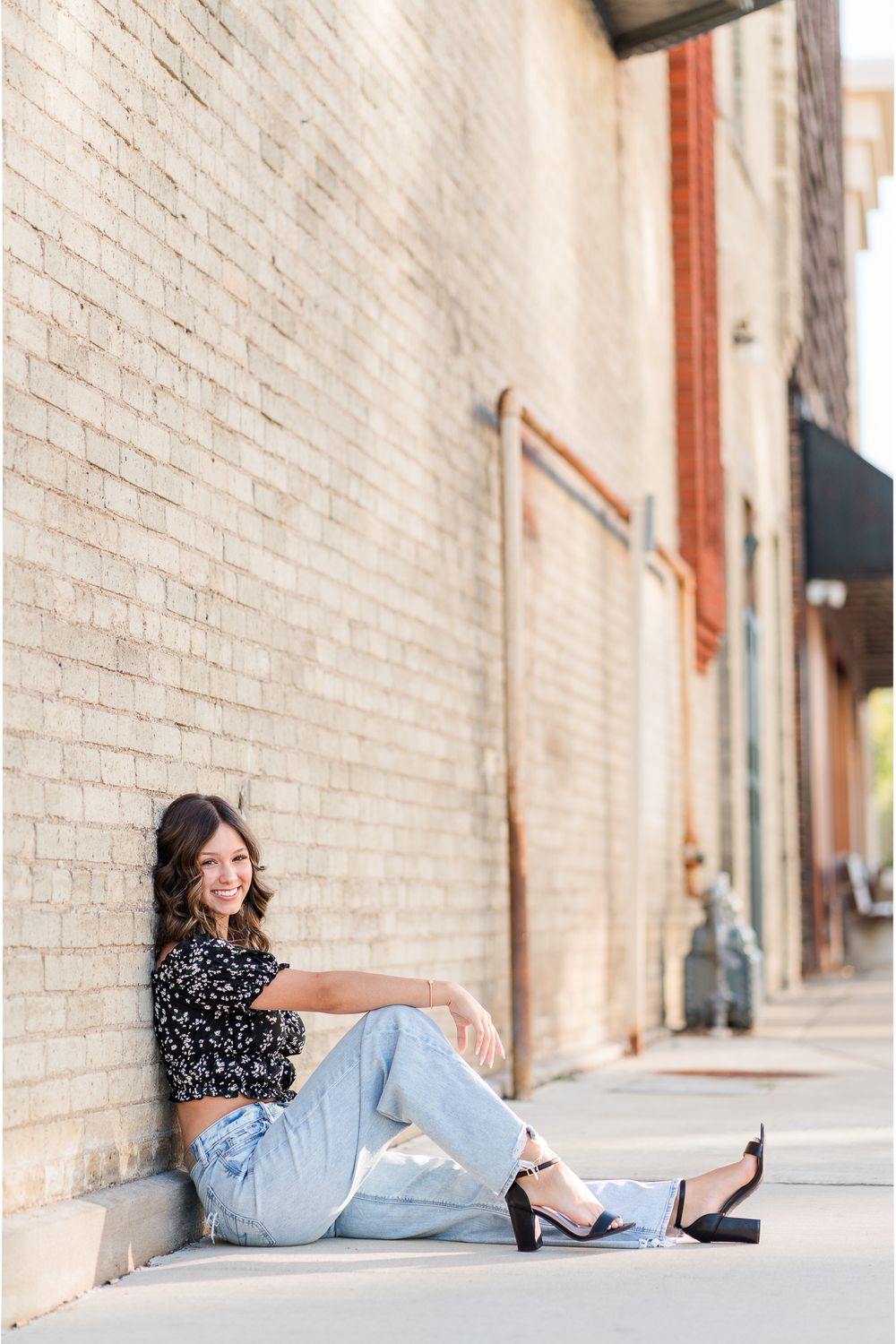 A casual fashion pose against a brick wall wearing denim and a patterned top.