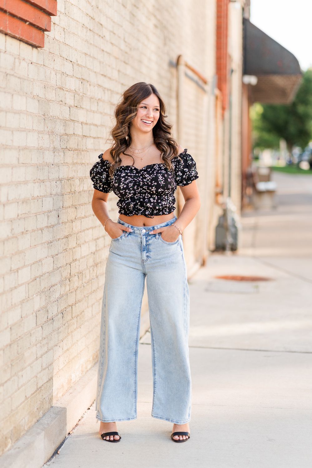 Street style fashion shot featuring wide-leg jeans and a floral crop top near brick walls.