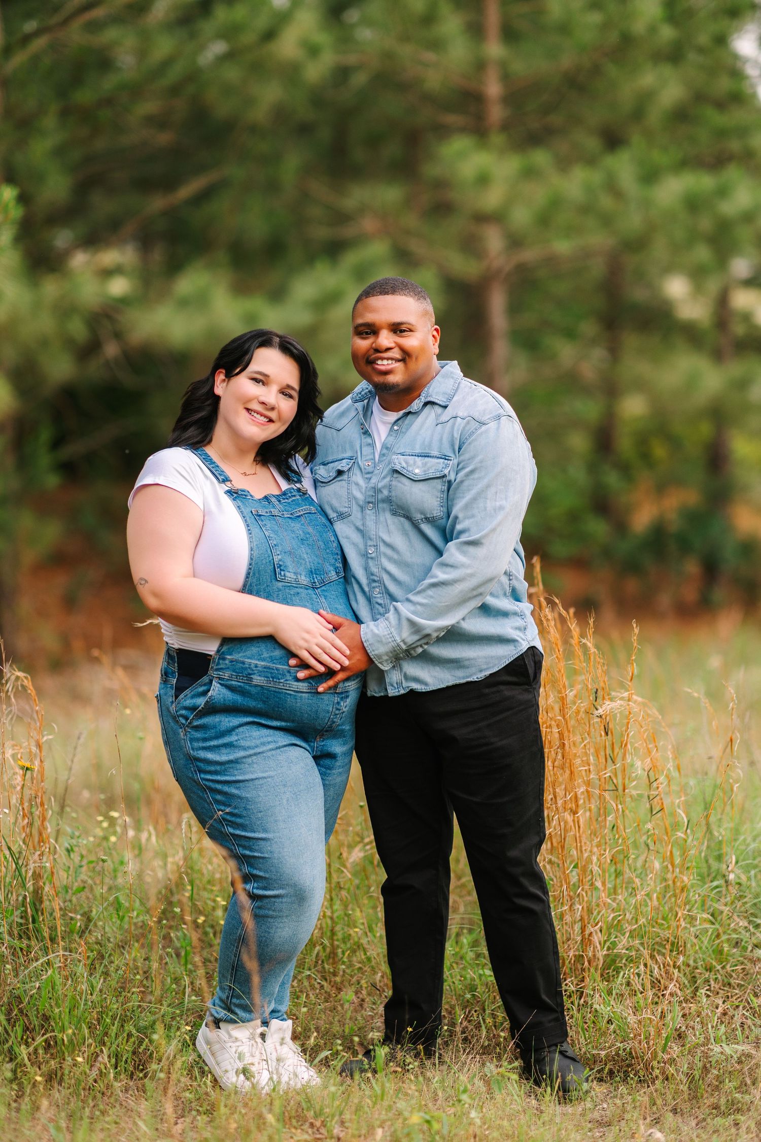 A couple in matching denim outfits share intimate moments in a field of tall grass during a photoshoot session.