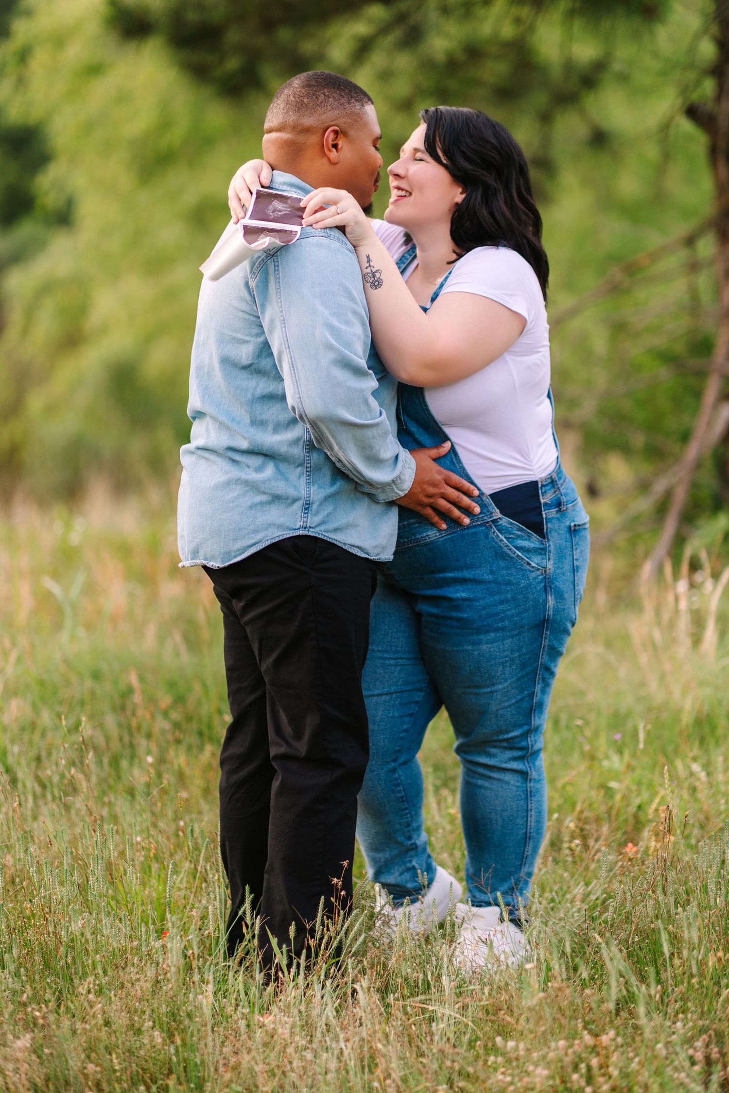 Loving couple embraces in tall grass during golden hour maternity photography session.