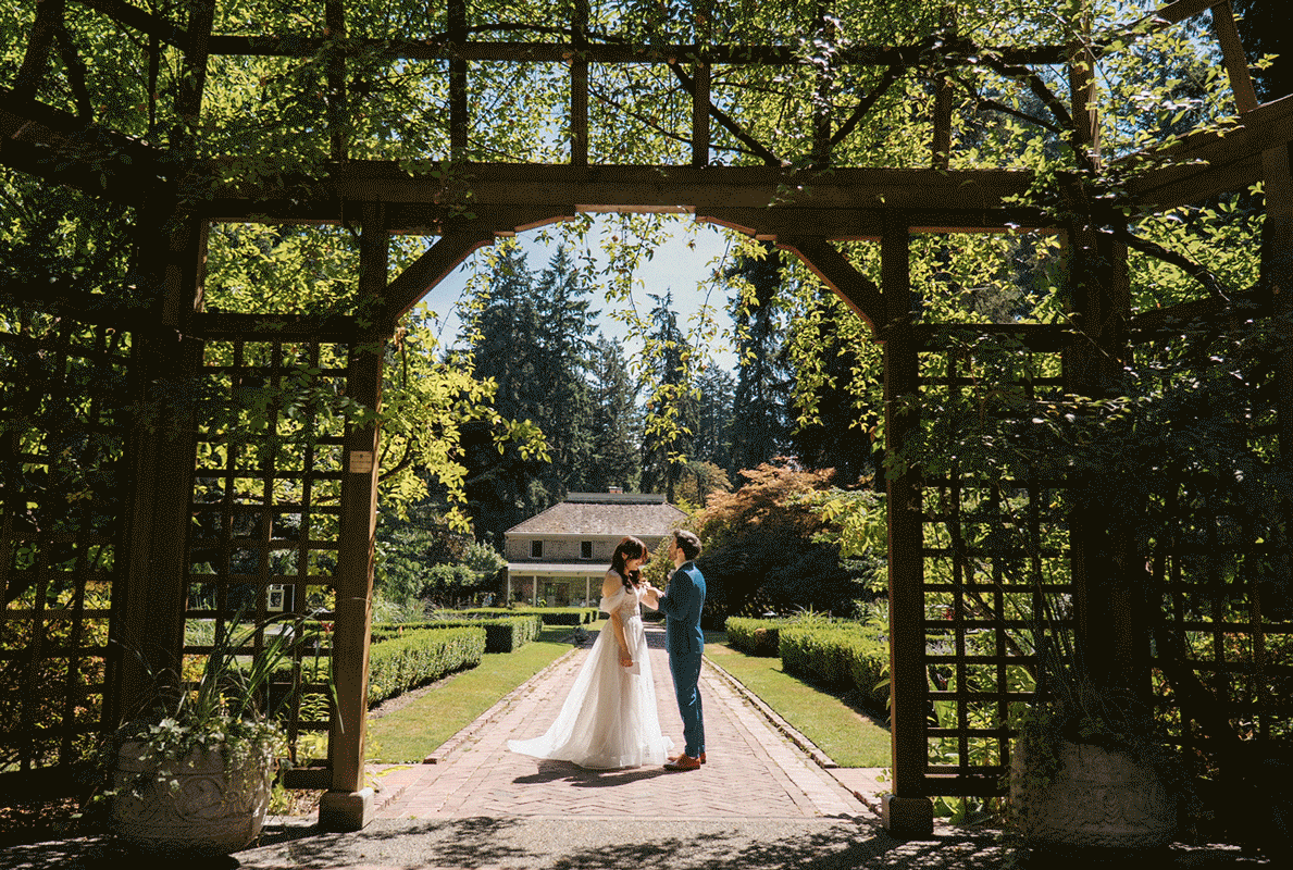 A couple walks through a lush garden archway tunnel covered in greenery and flowers during their outdoor wedding.