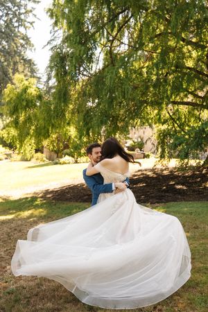 Wedding couple in embrace poses for romantic photo series under weeping willow trees at sunset.
