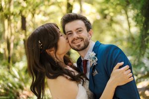 A couple shares an intimate moment during an outdoor photo session with golden sunlight filtering through trees.