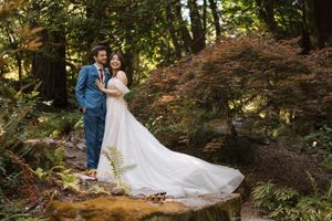Romantic wedding couple poses together in a lush wooded area with autumn foliage in the background.