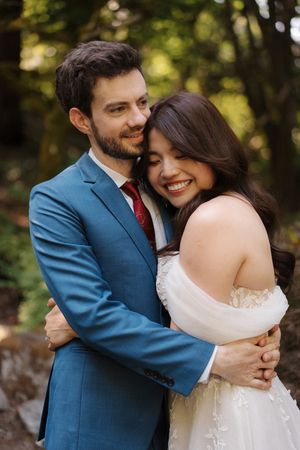 A tender moment between newlyweds as they embrace outdoors in a natural setting.