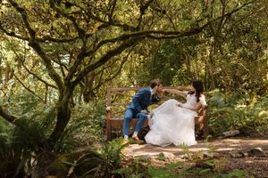 A couple poses among lush trees in a wooded area during a wedding photoshoot session.
