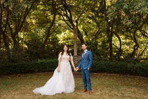 Two well-dressed people share romantic photos in a sunlit wooded outdoor setting.