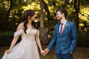 A couple in wedding attire hold hands and share romantic moments in a sunlit outdoor garden setting.