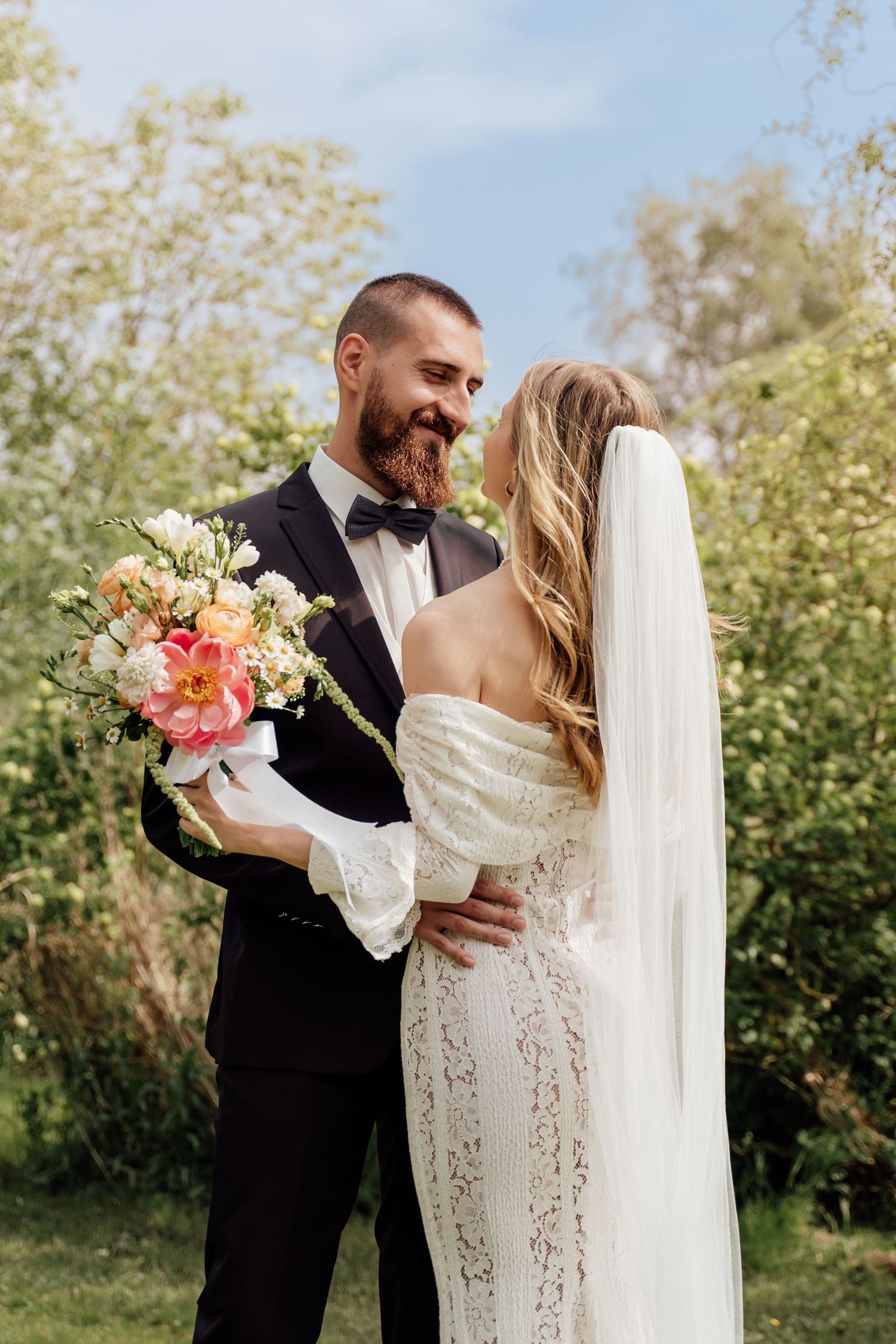 A wedding couple shares an intimate moment outdoors surrounded by greenery on their special day.