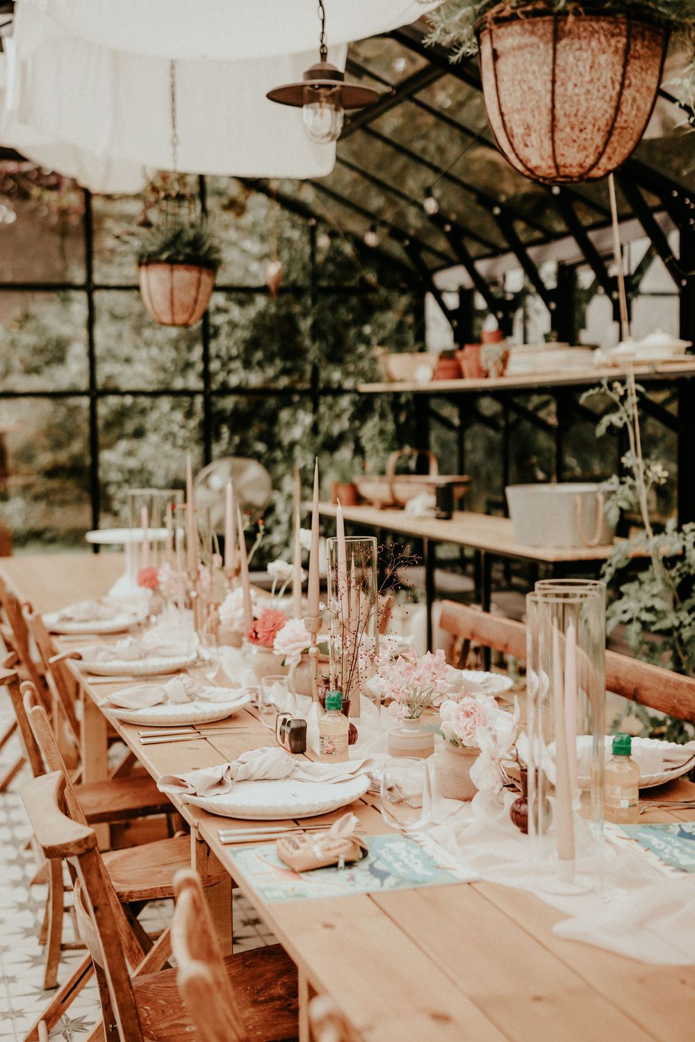 Elegant rustic wedding reception table setting with wooden chairs and hanging lanterns in a greenhouse venue.