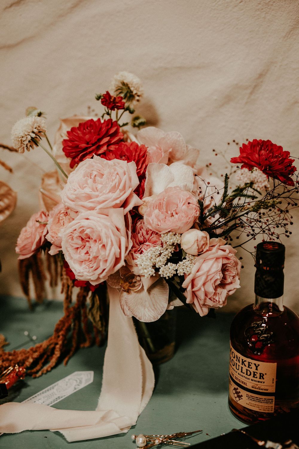 Romantic floral arrangement with soft pink roses and red flowers in vintage brown bottles on moody dark surface.