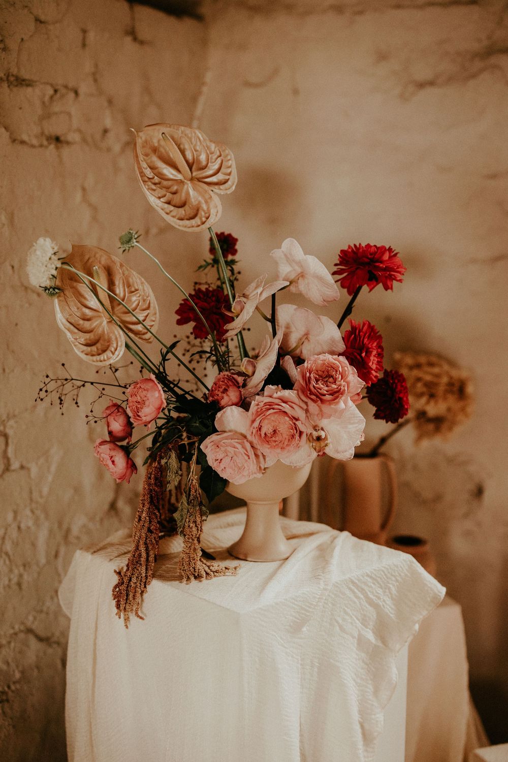 Romantic floral arrangement with pink and red blooms in white vases against a textured vintage wall backdrop.