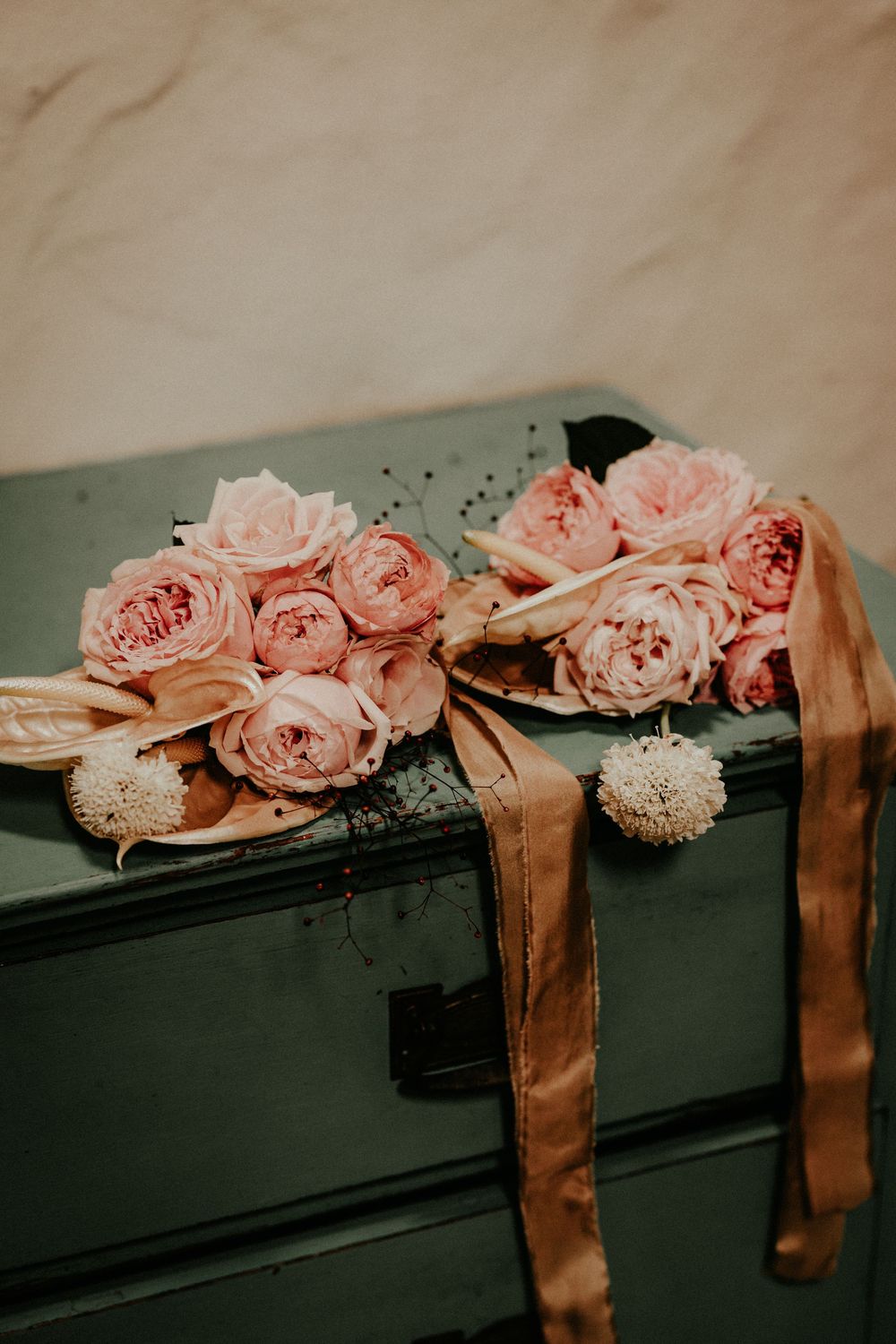 Pink roses and white flowers lay elegantly arranged along a dark surface with copper-colored silk ribbon.