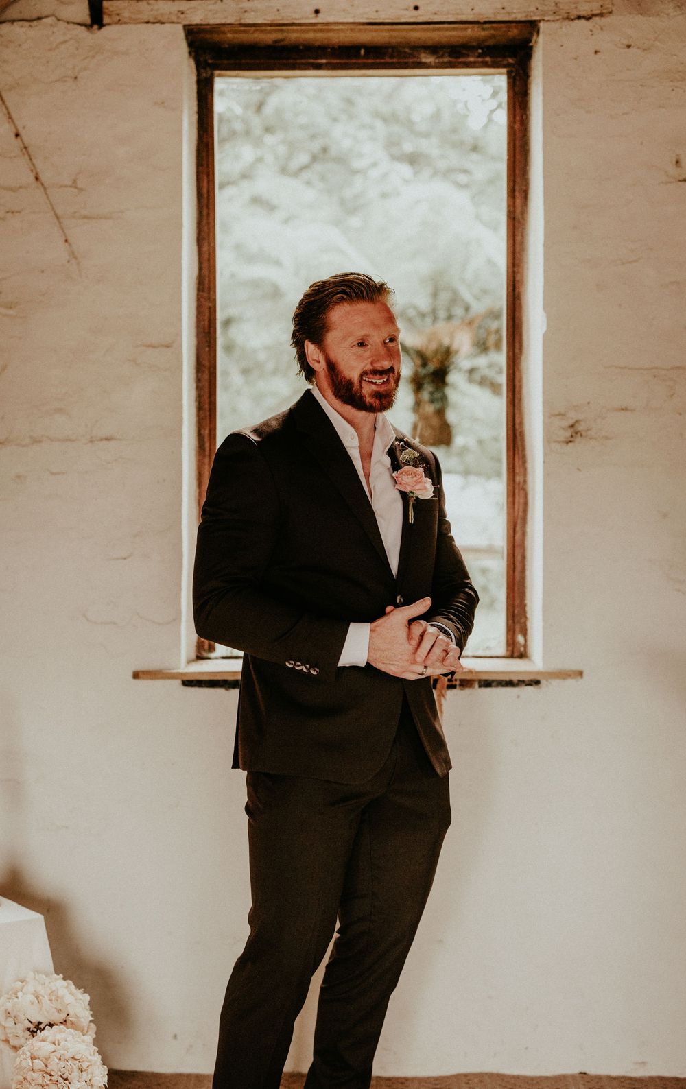 A wedding sequence showing a person in a black suit holding a bouquet while standing in a rustic white room.