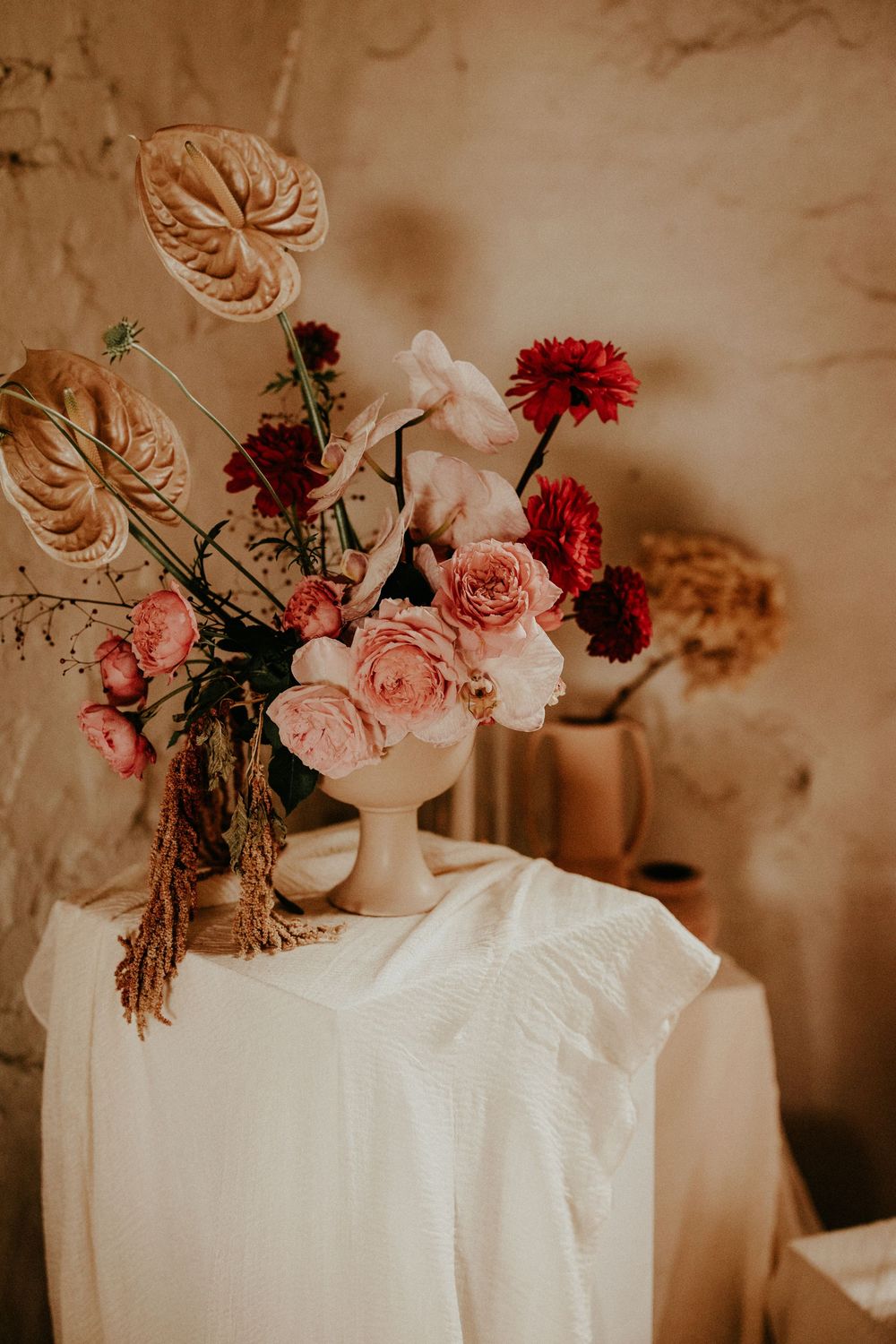 An elegant arrangement of pink roses and red dahlias with dried foliage creates a warm vintage atmosphere.