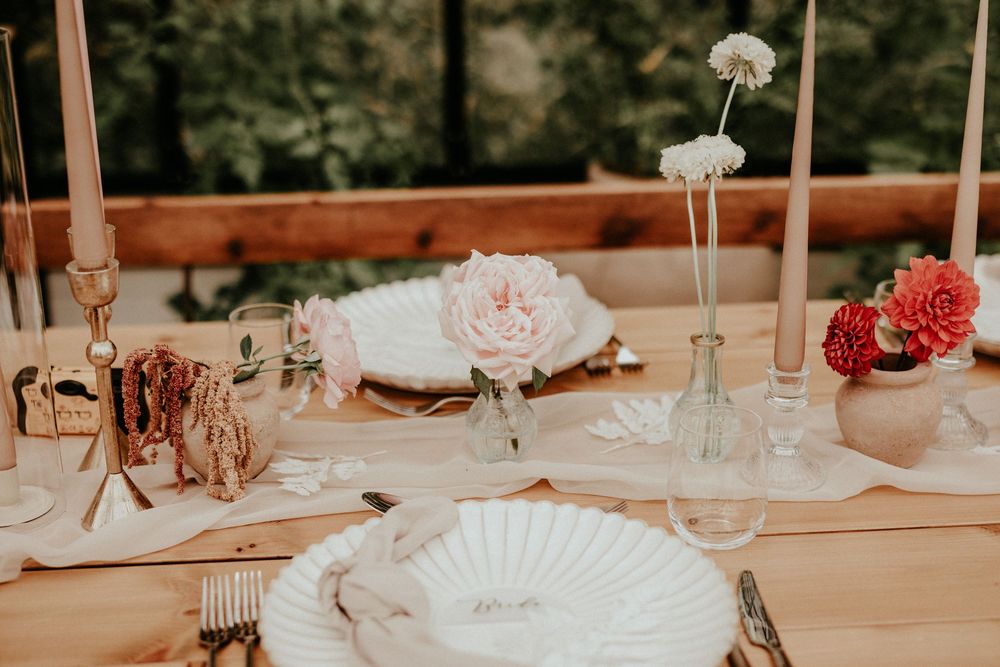 Elegant wedding table setting with dusty pink roses, white fans, and soft candlelight glowing on cream tablecloth.