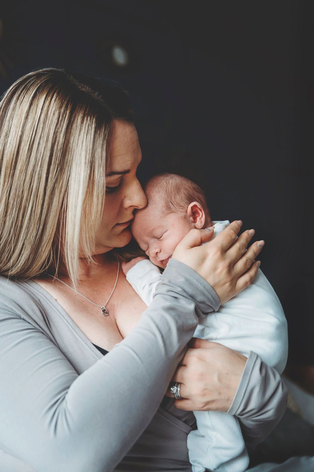 A mother in a gray sweater shares tender moments kissing her baby in a series of intimate portraits.
