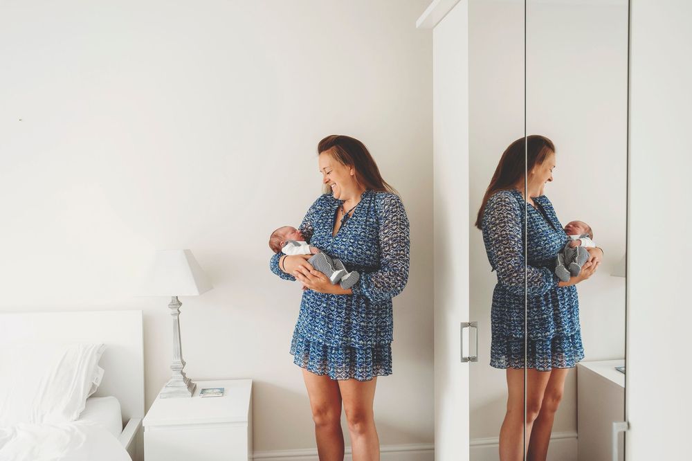Woman in blue floral dress taking mirror selfies from different angles in white room.