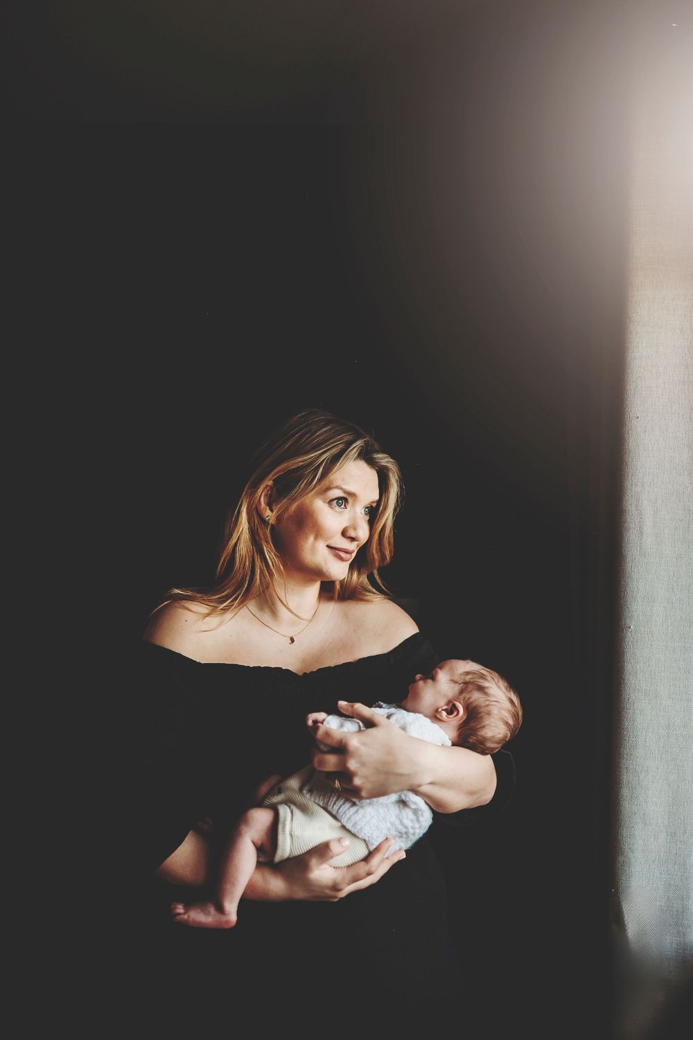 A dark and moody series of photos showing a parent holding their newborn baby against black shadows and dramatic lighting.