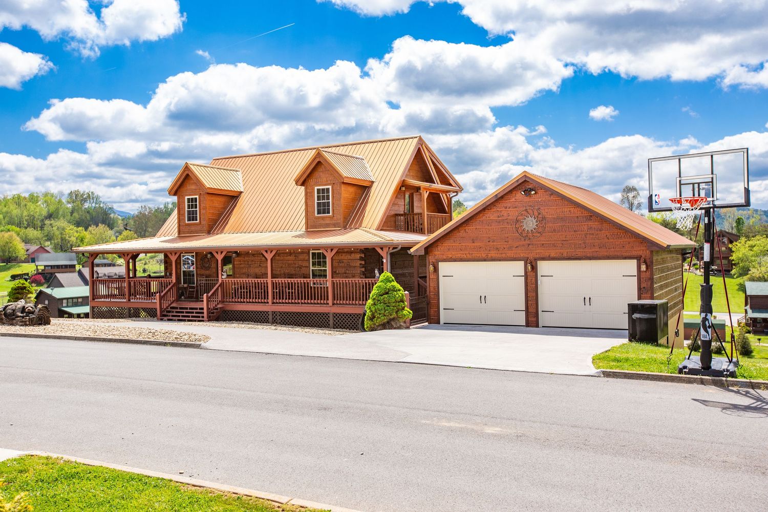 A panoramic view of a modern log cabin resort with multiple buildings and parking areas under a blue cloudy sky.