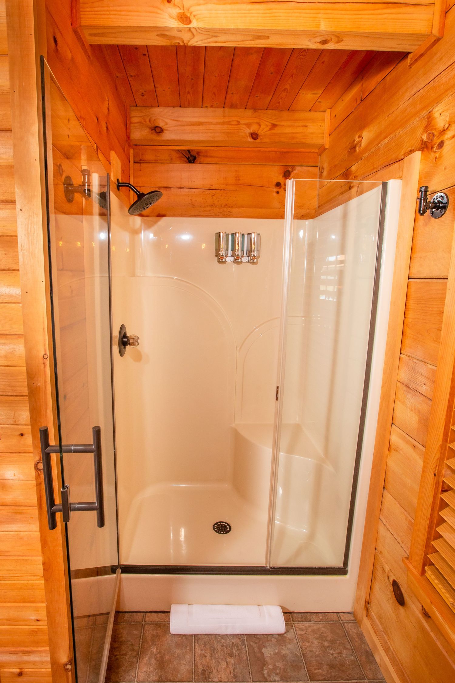 Modern white shower enclosure with glass doors in a log cabin bathroom featuring pine wood walls.