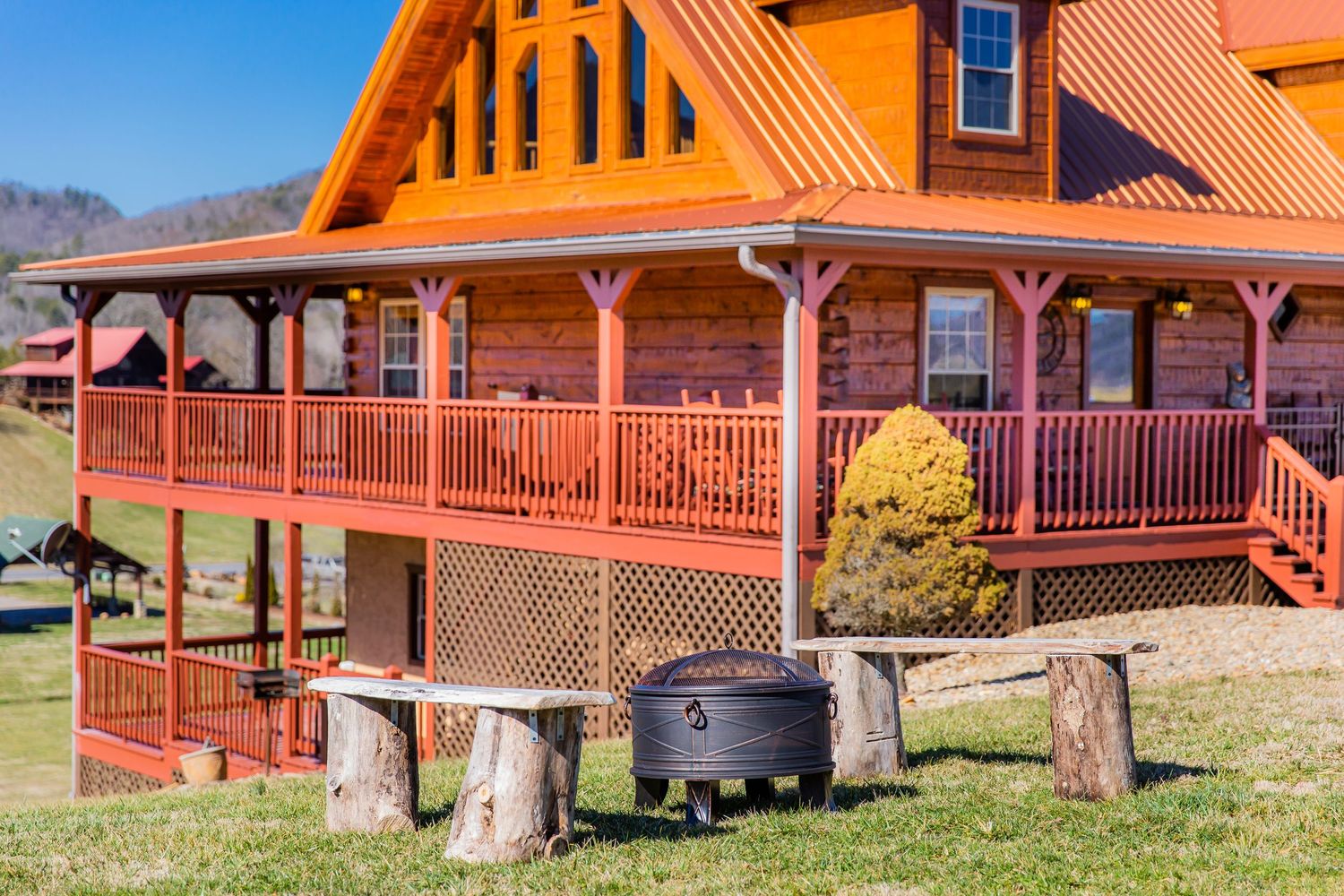 Log cabin vacation rentals with red trim nestled in a scenic mountain valley with wooden decks and rustic landscaping.