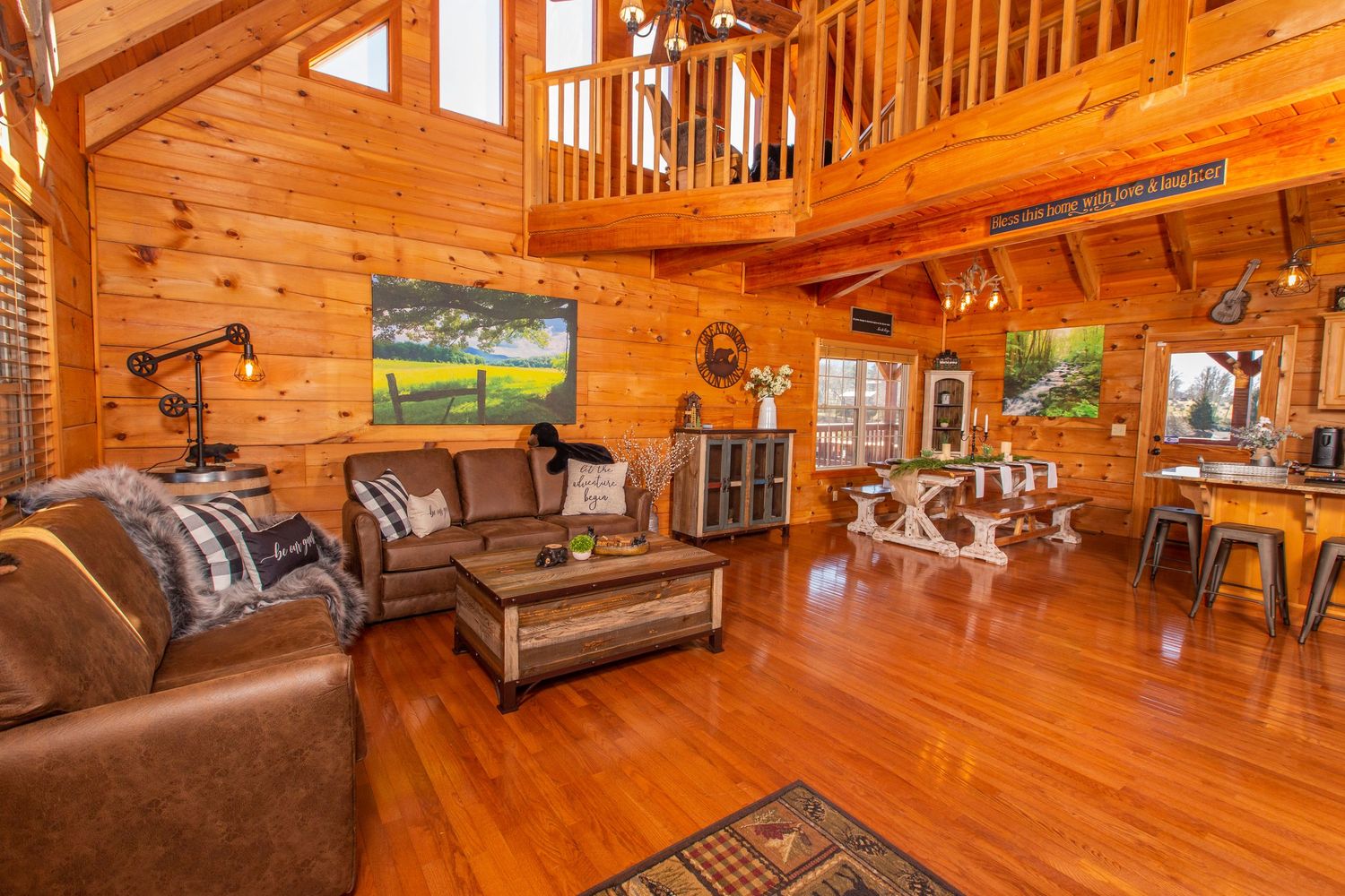 Spacious log cabin living room with vaulted ceiling, leather furniture, and loft area.