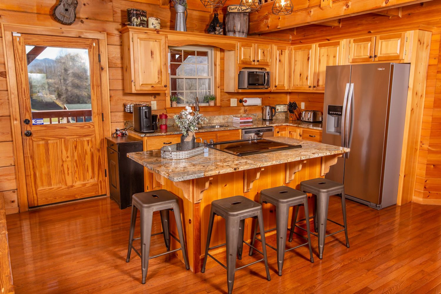 Rustic wooden kitchen interior with knotty pine cabinets, granite island, metal barstools and hardwood flooring.
