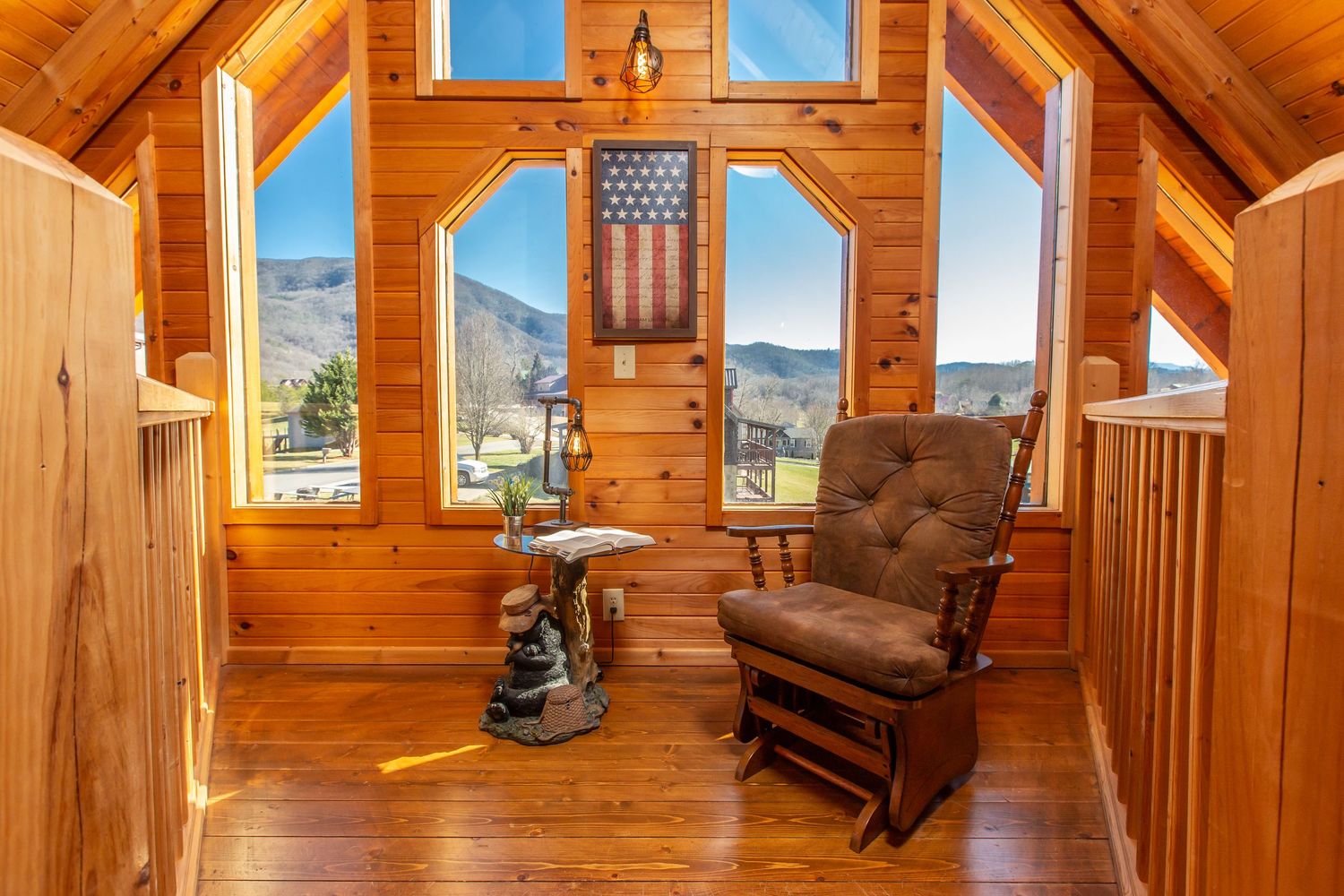 Cozy log cabin interior with wooden walls, ceiling fan, and large windows showcasing mountain views.