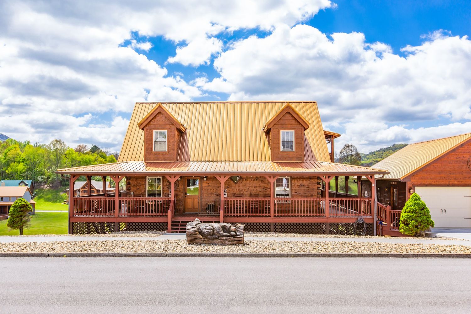 A series of brown wooden log cabin buildings with copper roofs set against a bright blue sky with white clouds.