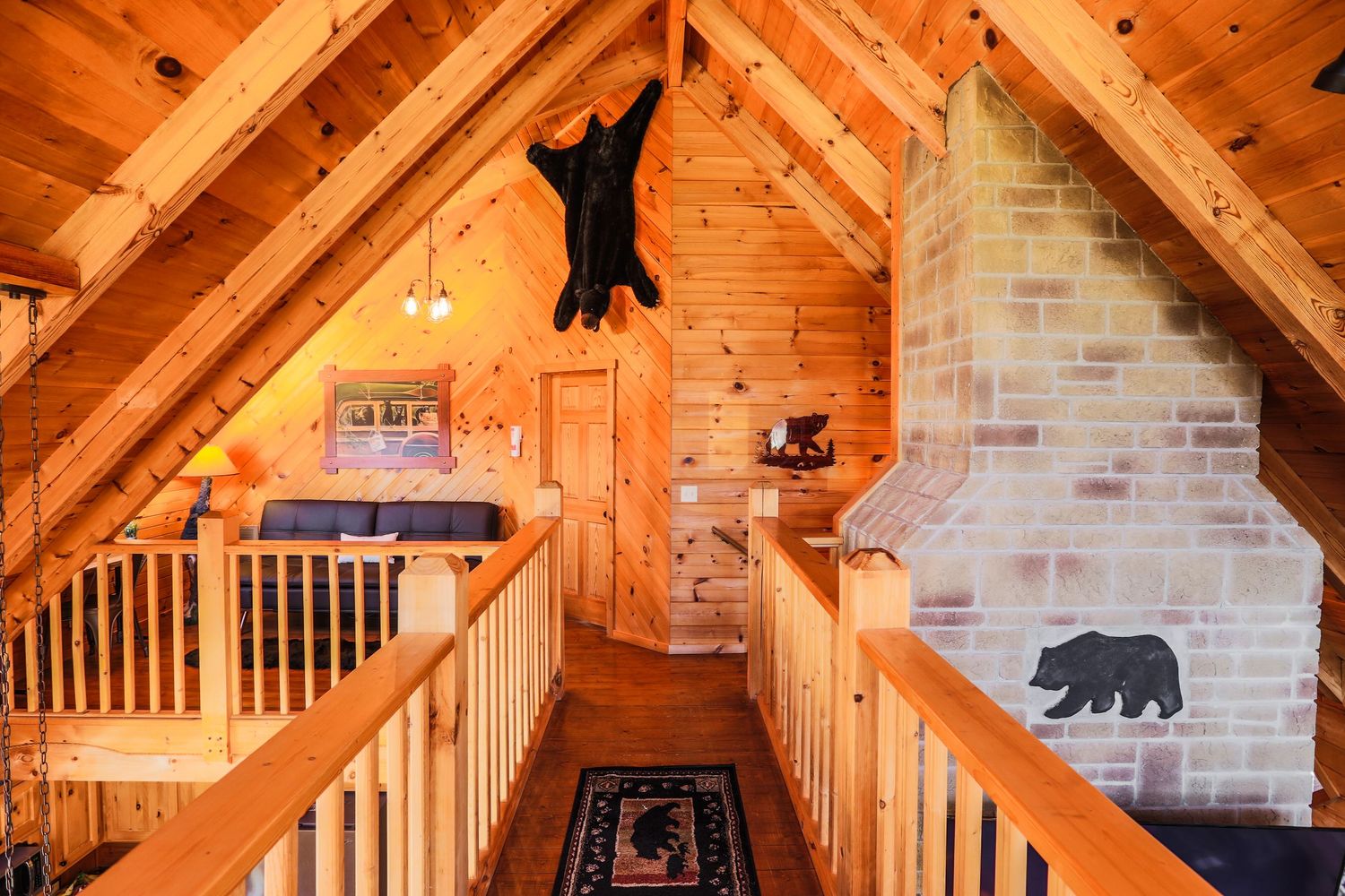 Rustic log cabin loft interior with exposed wood beams, stone chimney, and black bear silhouette decorations on the wall.
