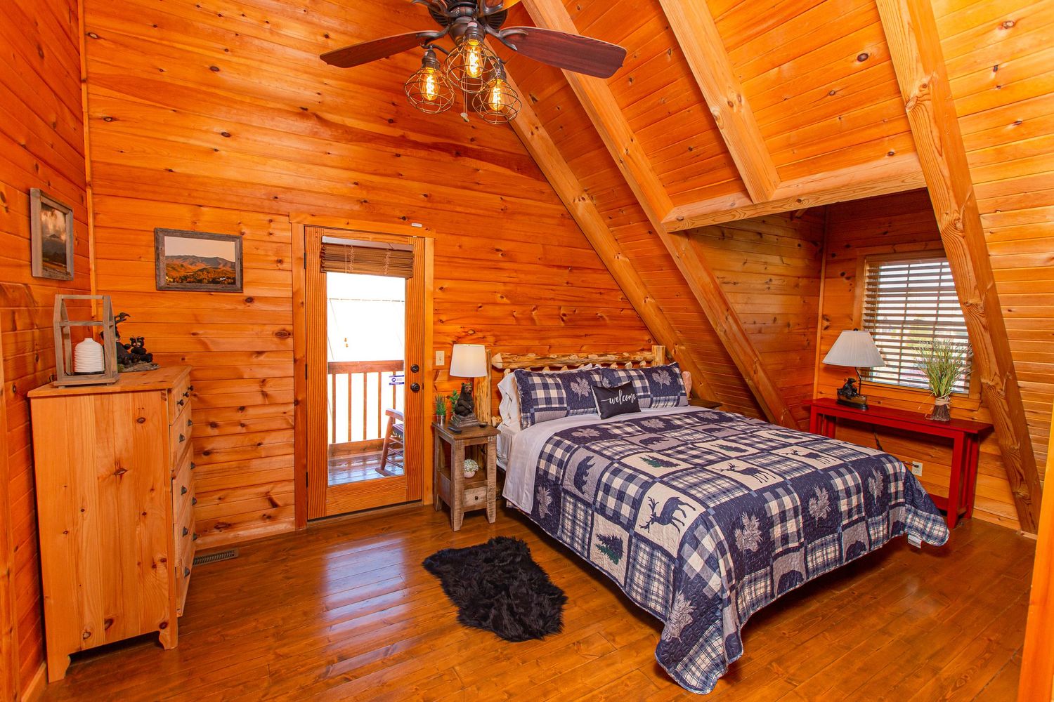 Rustic bedroom with wood paneled walls, plaid bedding, and natural light streaming through windows.