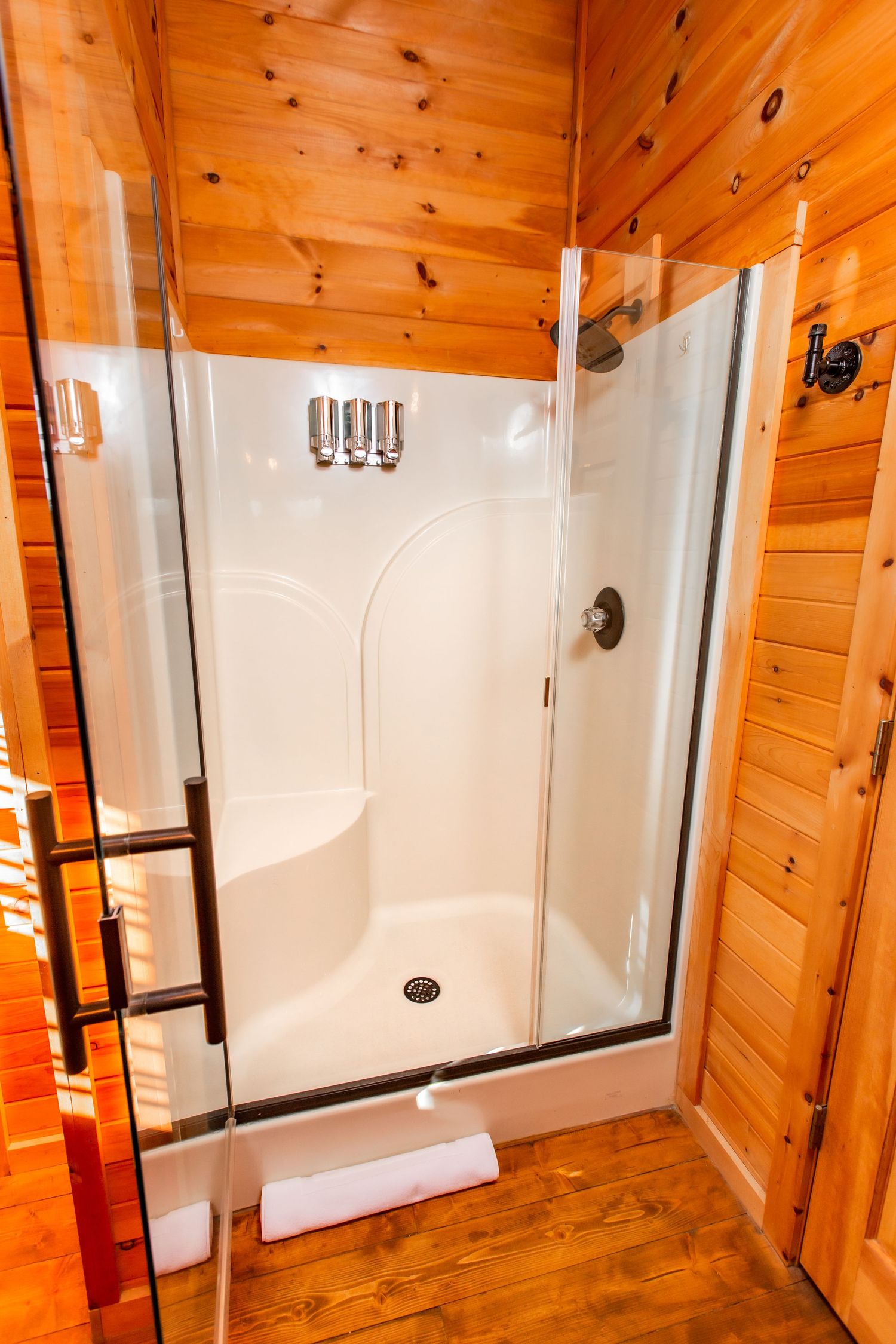 Modern white shower enclosure contrasting with warm wood paneled walls in a cabin bathroom.