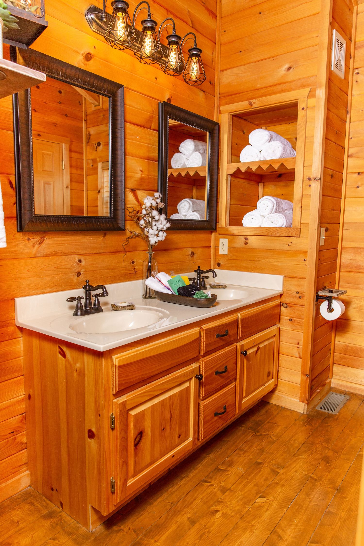 Luxurious log cabin bathroom with wooden vanity, double sinks, and warm lighting reflecting off pine walls.