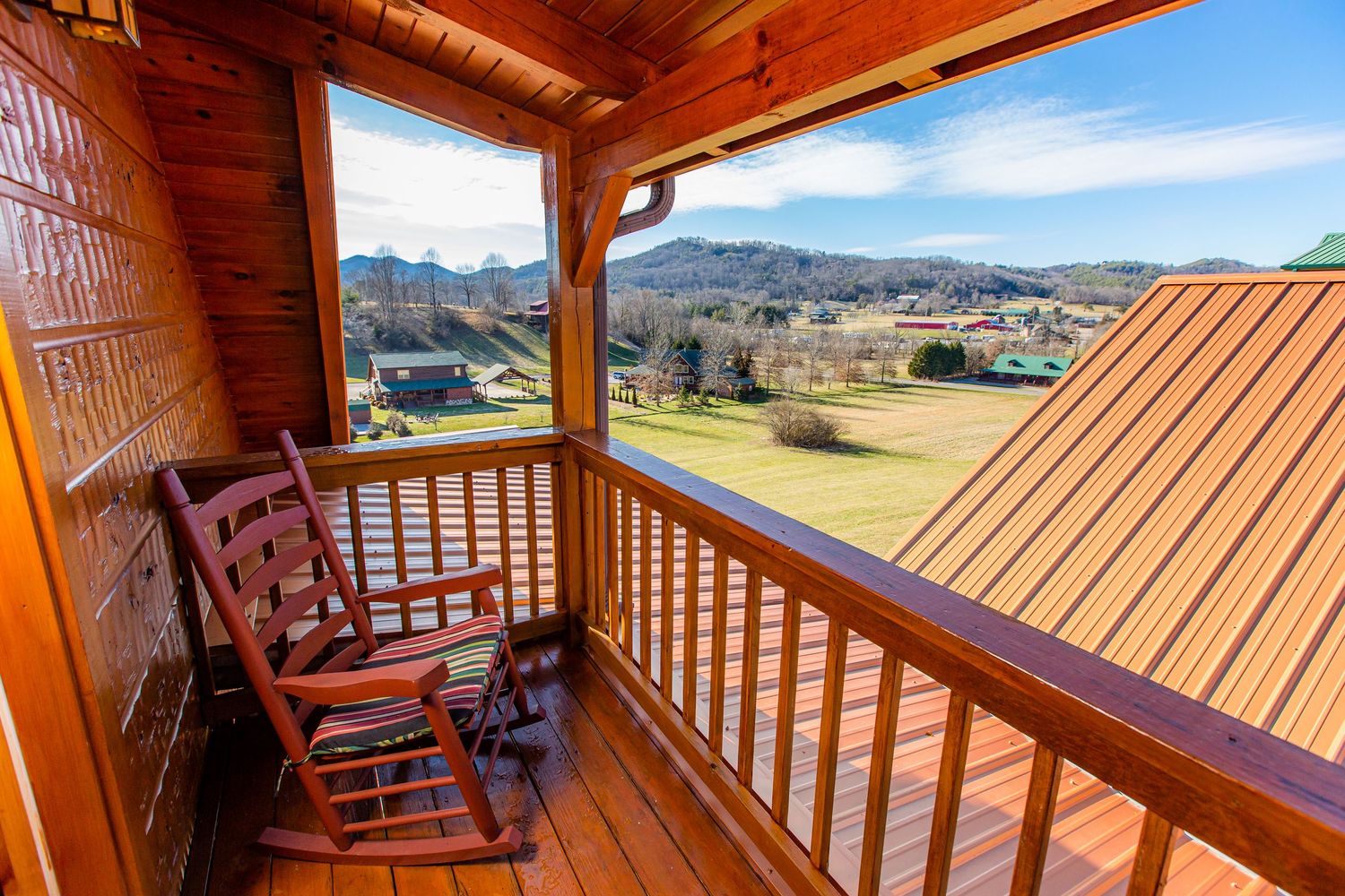 Panoramic view of mountains and valley from a wooden deck with railing at sunset.