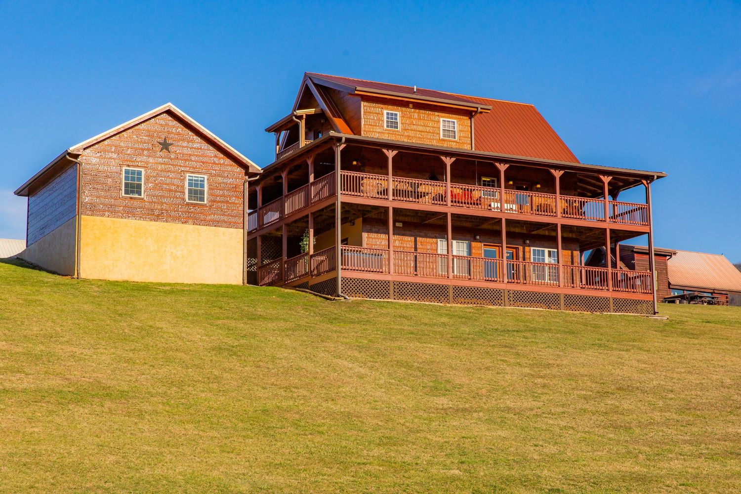 Panoramic view of rustic log cabin lodges nestled on a grassy hillside under bright blue sky.
