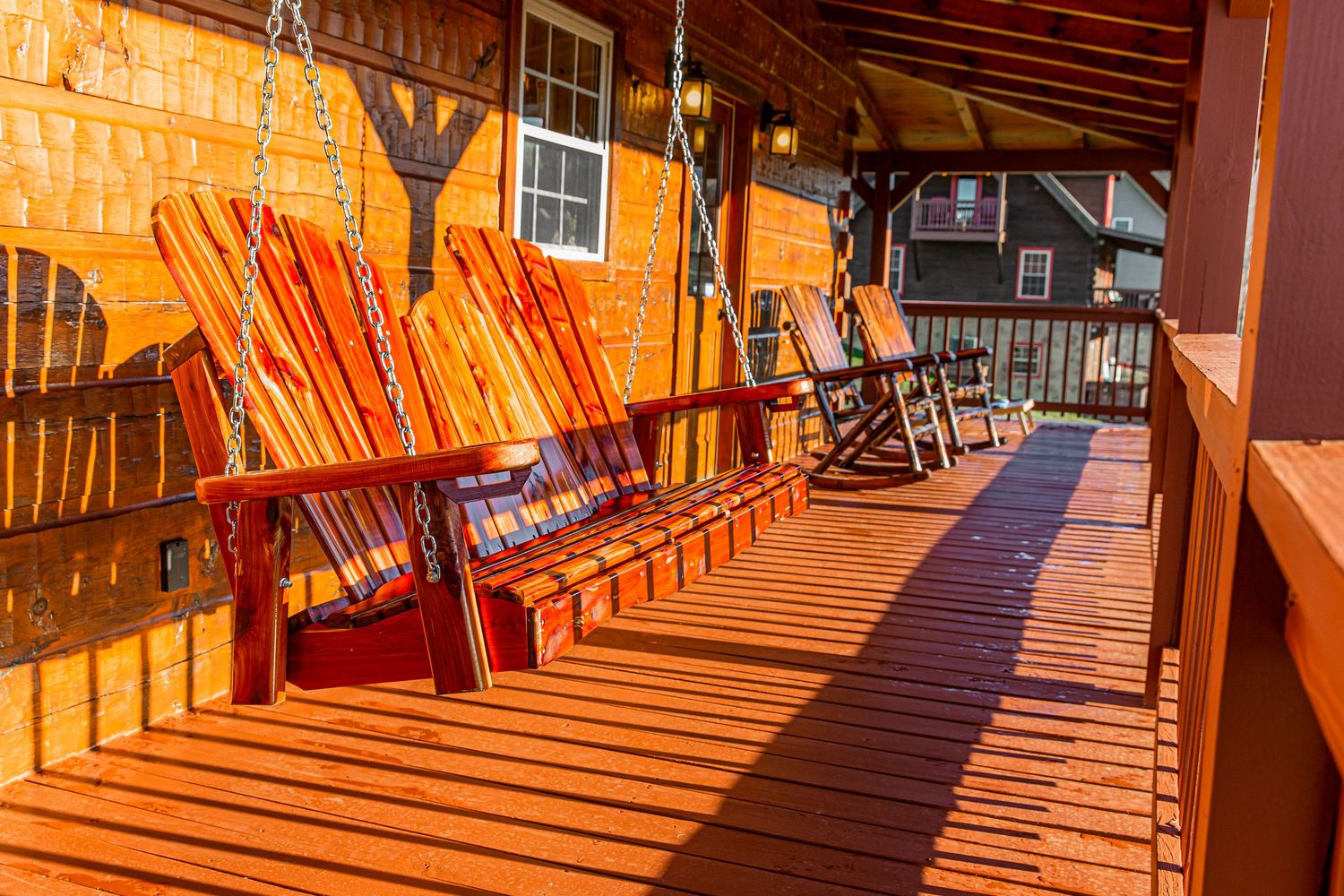 Sun-drenched wooden deck with rocking chairs casting long shadows through rustic cabin railings.
