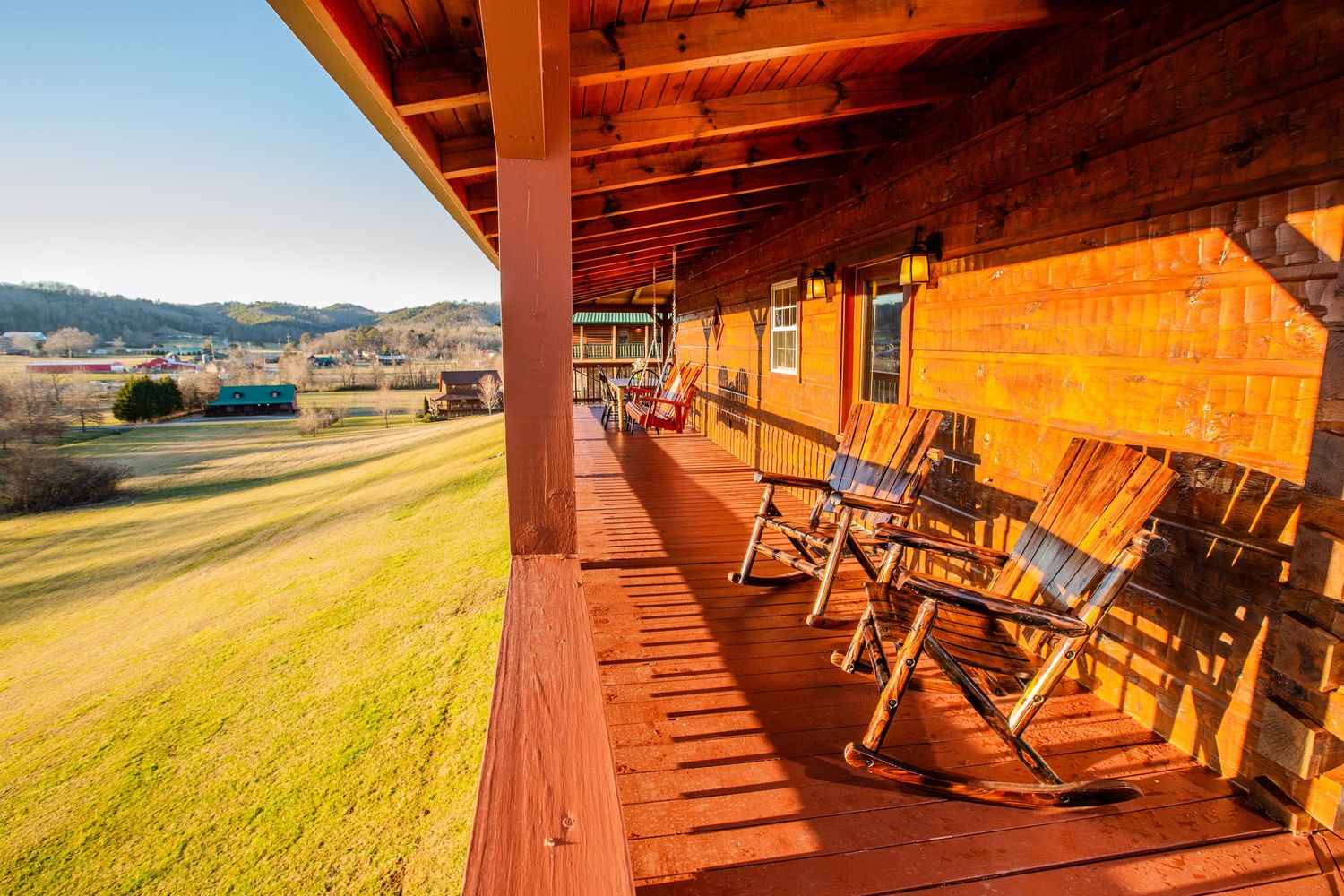 Rustic wooden deck with rocking chairs overlooking a scenic mountain landscape at sunset.