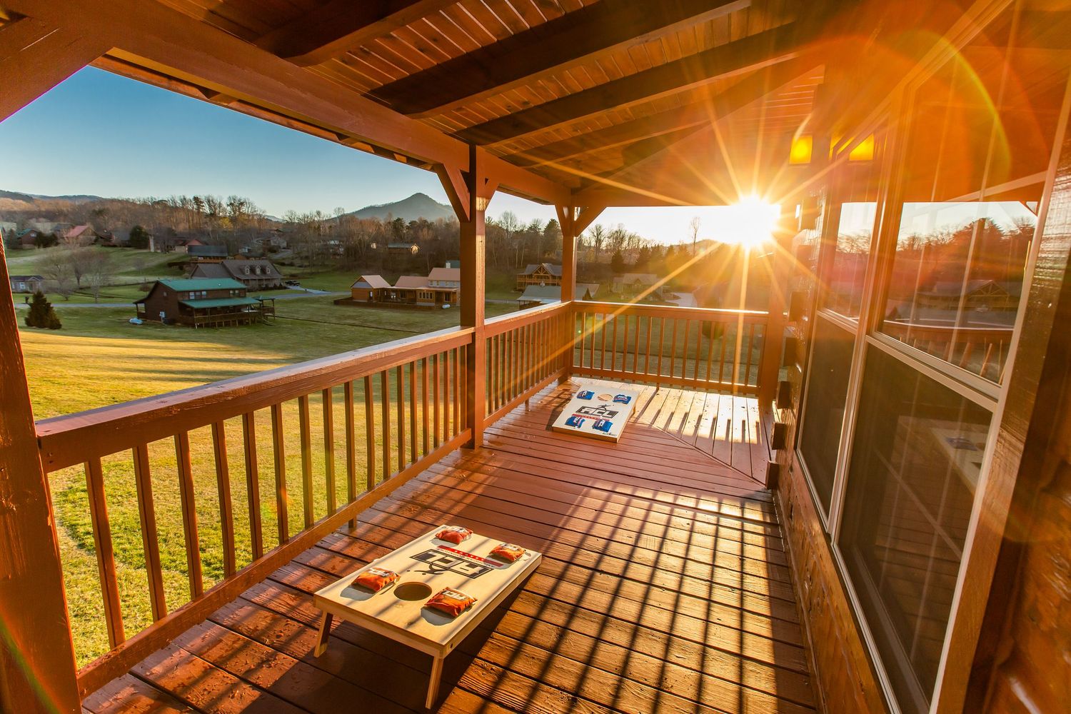 Spacious covered deck with wooden railing overlooking scenic mountain landscape at dusk.