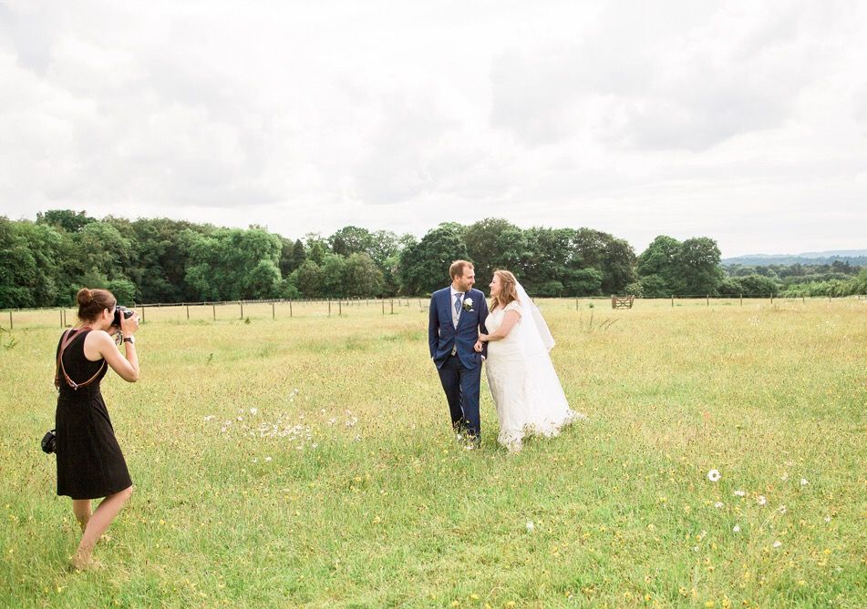 Photographer capturing wedding couple in sunny meadow with wildflowers.